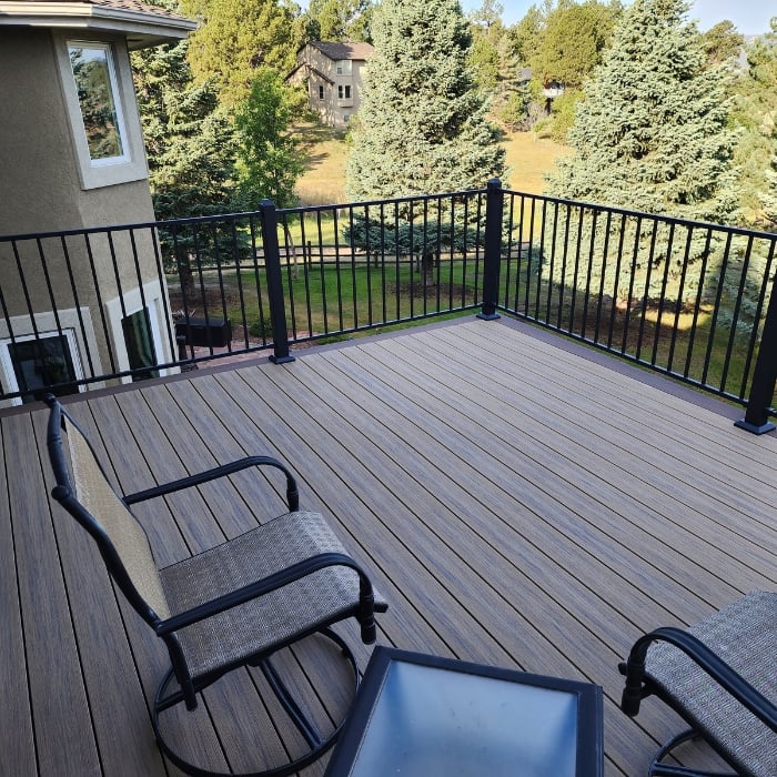Grey Deck Overlooking Lush Green Backyard with Chairs and Black Railing